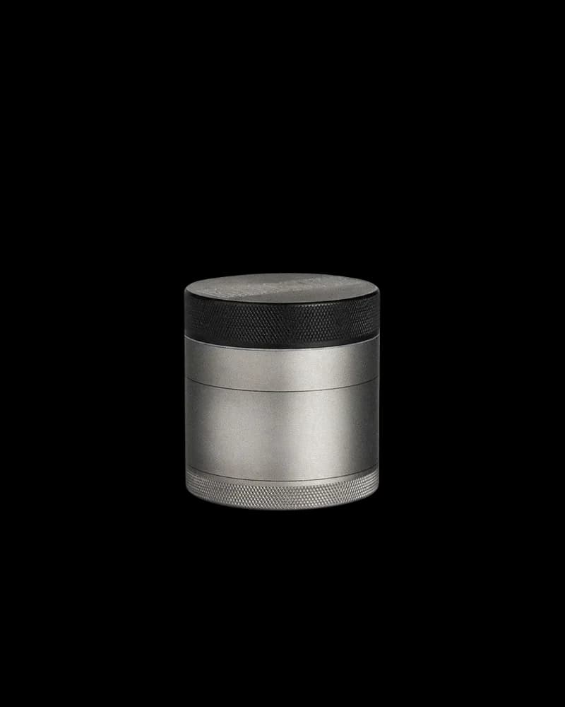 Four-piece cannabis grinder with black top cap, brushed aluminum body, and textured grip bands