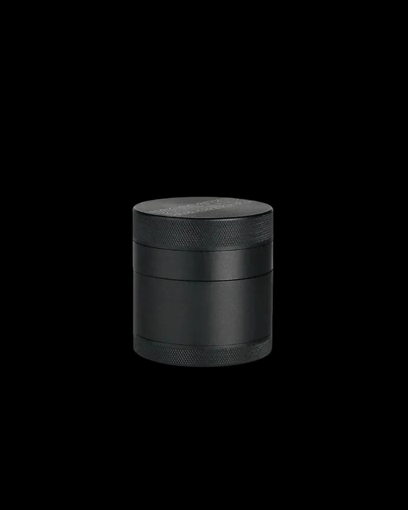 Four-piece black aluminum cannabis grinder with textured top and bottom rings, middle band, and grinding chamber